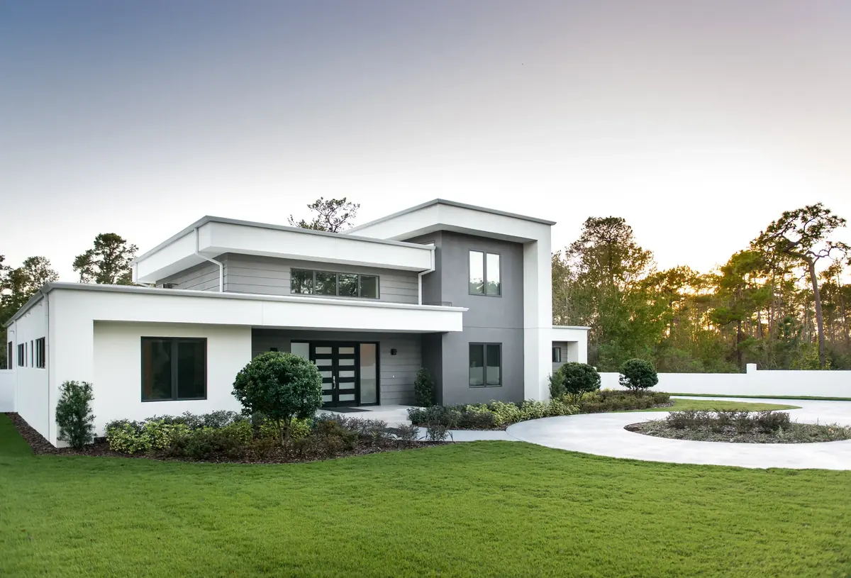 Modern two-storey house at dusk, seen from the front garden with the driveway curving past